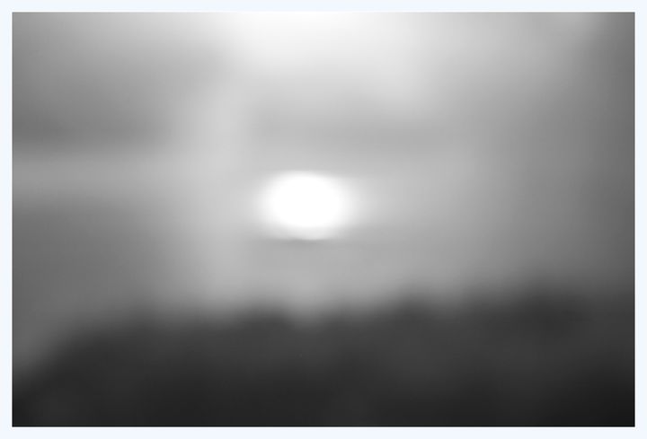 An out-of-focus image of what appears to be the sun above some trees.