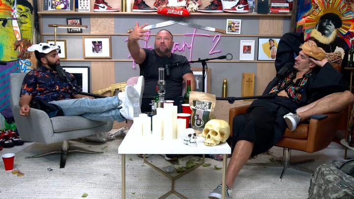 Alex Jones sitting in a podcast studio with Andrew Schulz and Akaash Singh.